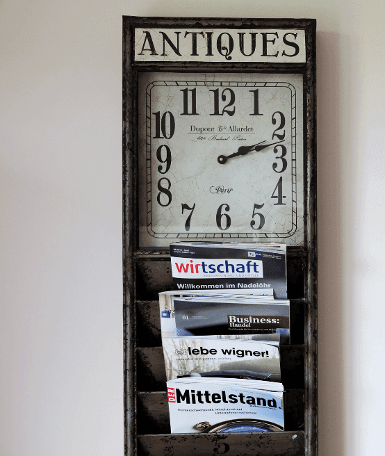 Antique-style wall-mounted magazine rack with a clock and various publications.